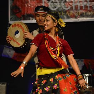 Tamang woman in traditional dress performing Tamang Selo dance with a damphu drum player behind her at a cultural event in Nepal