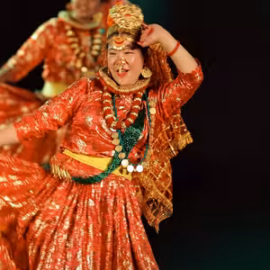 Nepali woman performing Maruni Dance in red and gold traditional costume performing a folk dance on stage, with swirling dress and heavy gold jewellery