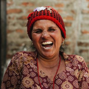 Nepali woman from the Bahun community laughing warmly, wearing traditional red headscarf and red bead necklace in Nepal