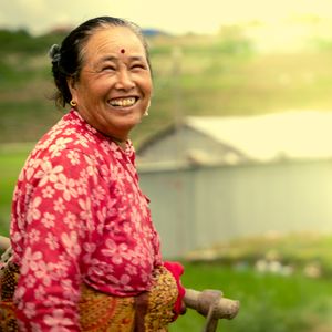 Smiling Nepali farmer woman in traditional red floral dress celebrating Rastriya Dhan Diwas in a rice field