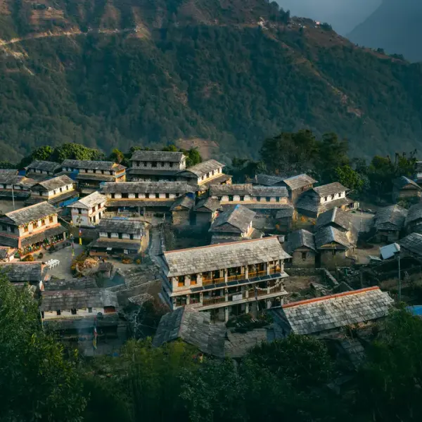 Village nestled in a lush green mountain landscape, with traditional stone houses.