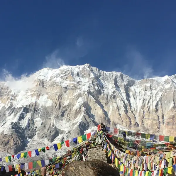 Prayer flags flutter before snow-capped Annapurna mountain range in Nepal.