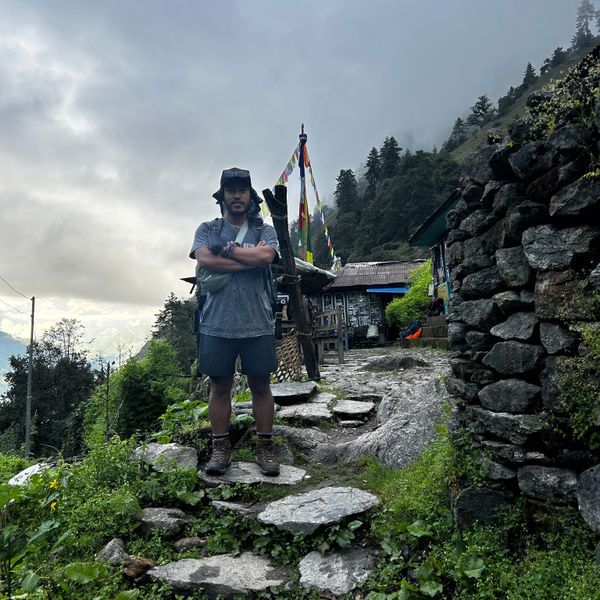 Trekker standing at a traditional stone gateway with prayer flags on the Langtang Valley Trek trail