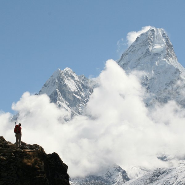 Trekker on ridge, Ama Dablam in clouds behind  Trekker on rocky ridge with Ama Dablam 6812m rising above clouds on Everest Base Camp Trek Nepal