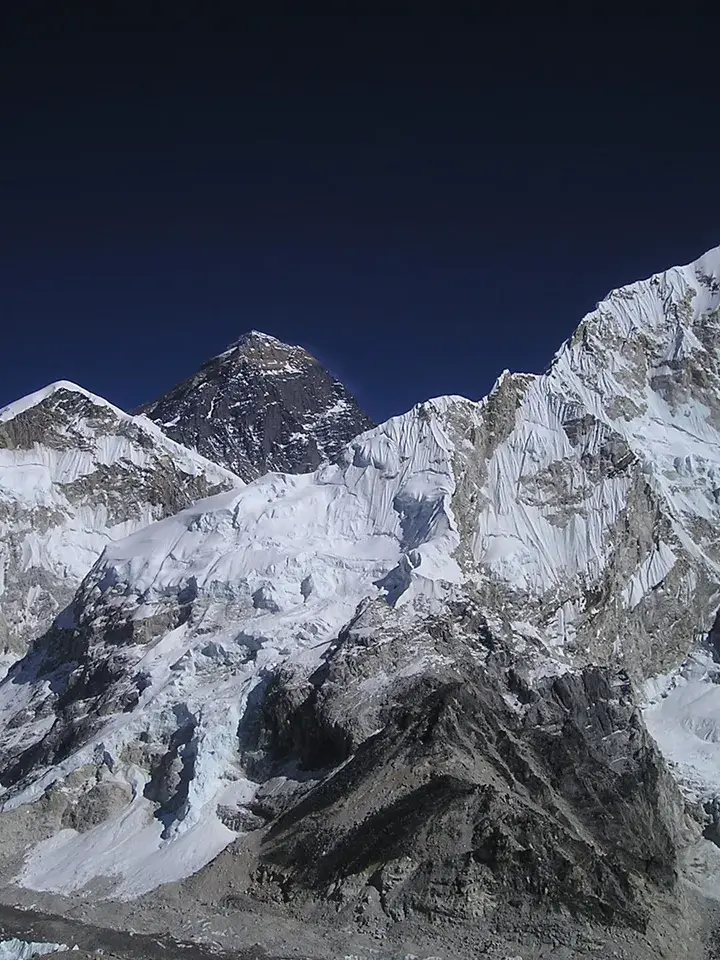 Sunlight halos the snow-covered summit of Mount Everest, highlighting its rugged Himalayan peak against a clear blue sky.