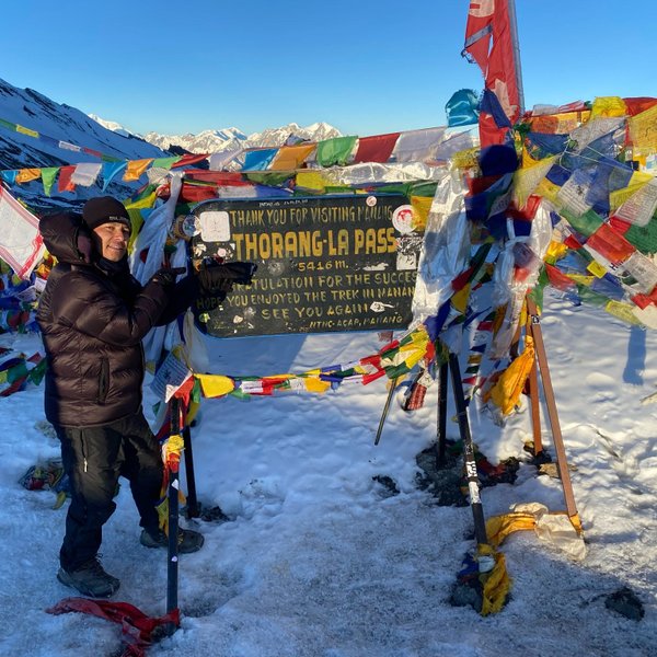 Trekker celebrating at Thorong La Pass surrounded by colorful prayer flags on the Annapurna Circuit Trek